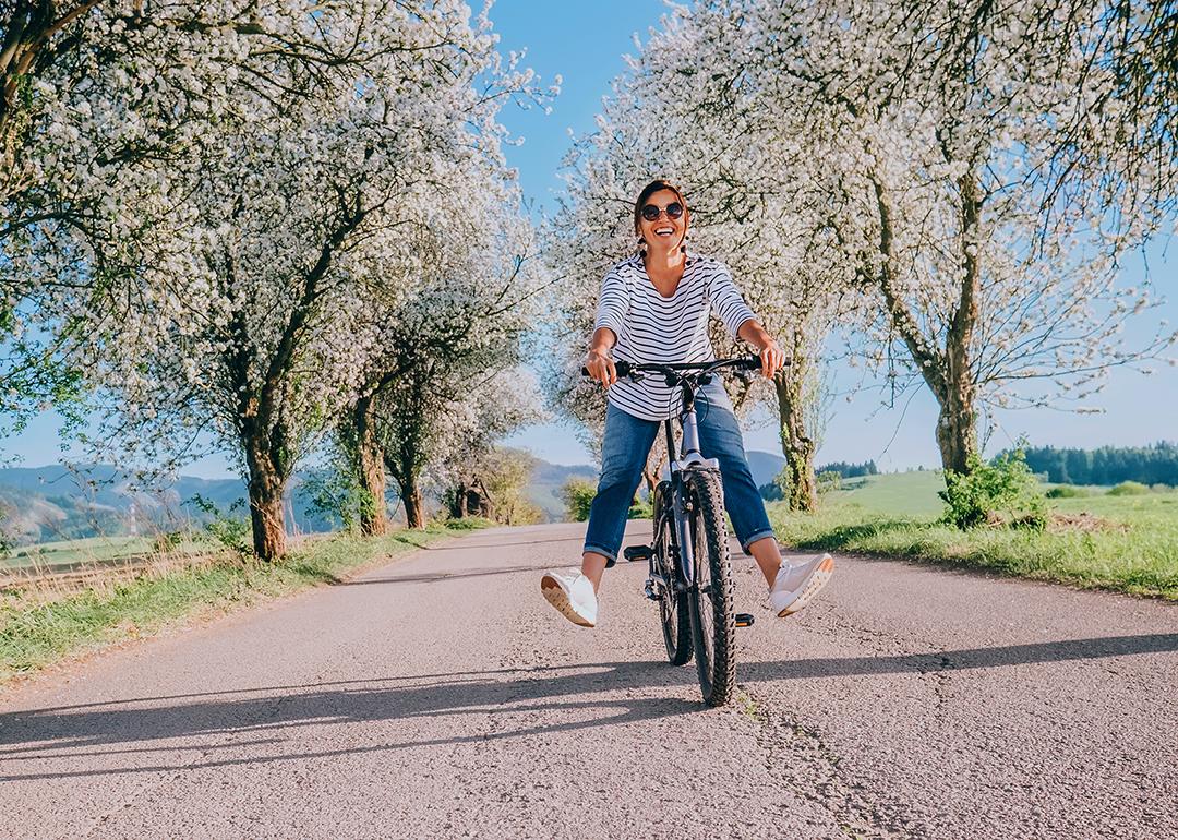 Happy smiling woman riding a bicycle under apple blossom trees.