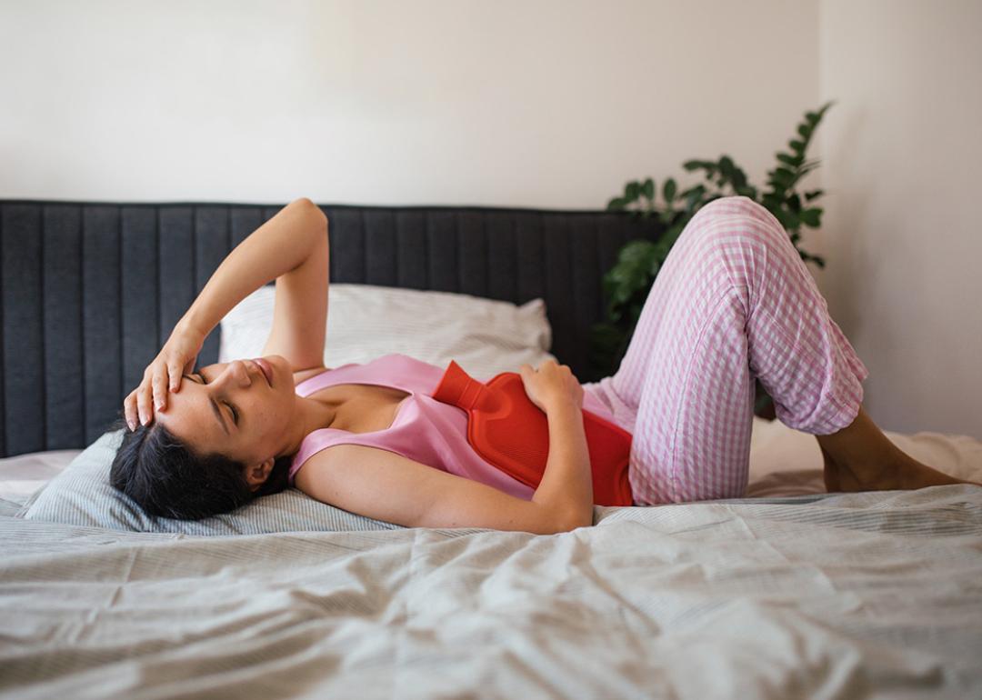 Woman lying in bed with a heat bag on abdomen; PMDD negatively affects many aspects of daily life.