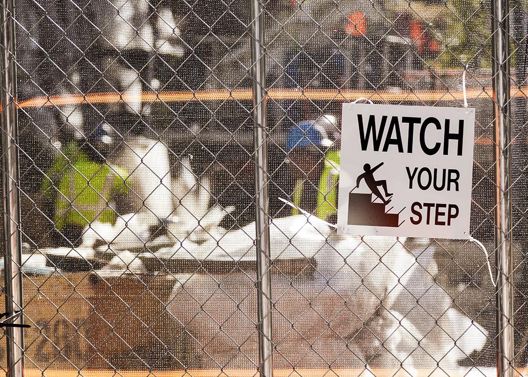 A 'watch your step' warning sign on the fence of a construction site.