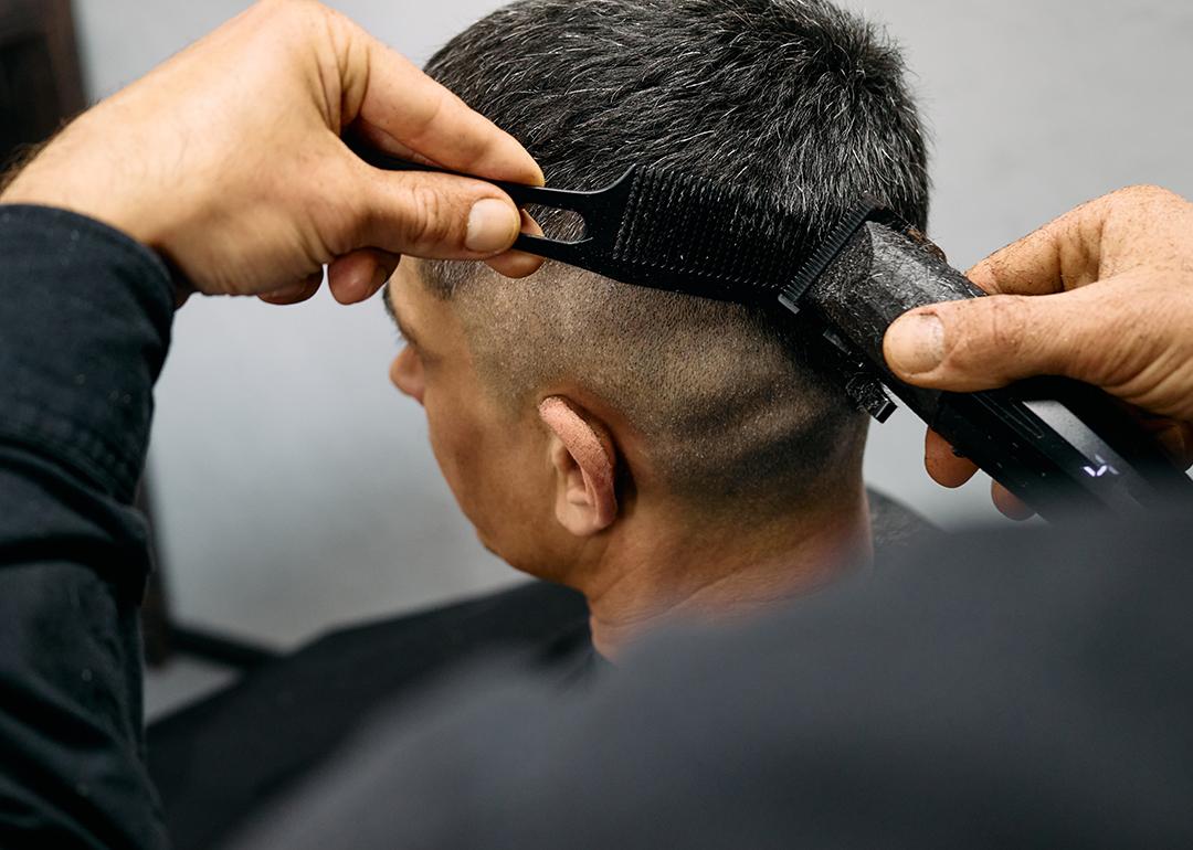 A barber expertly cuts a man's hair using clippers creating a smooth fade style.