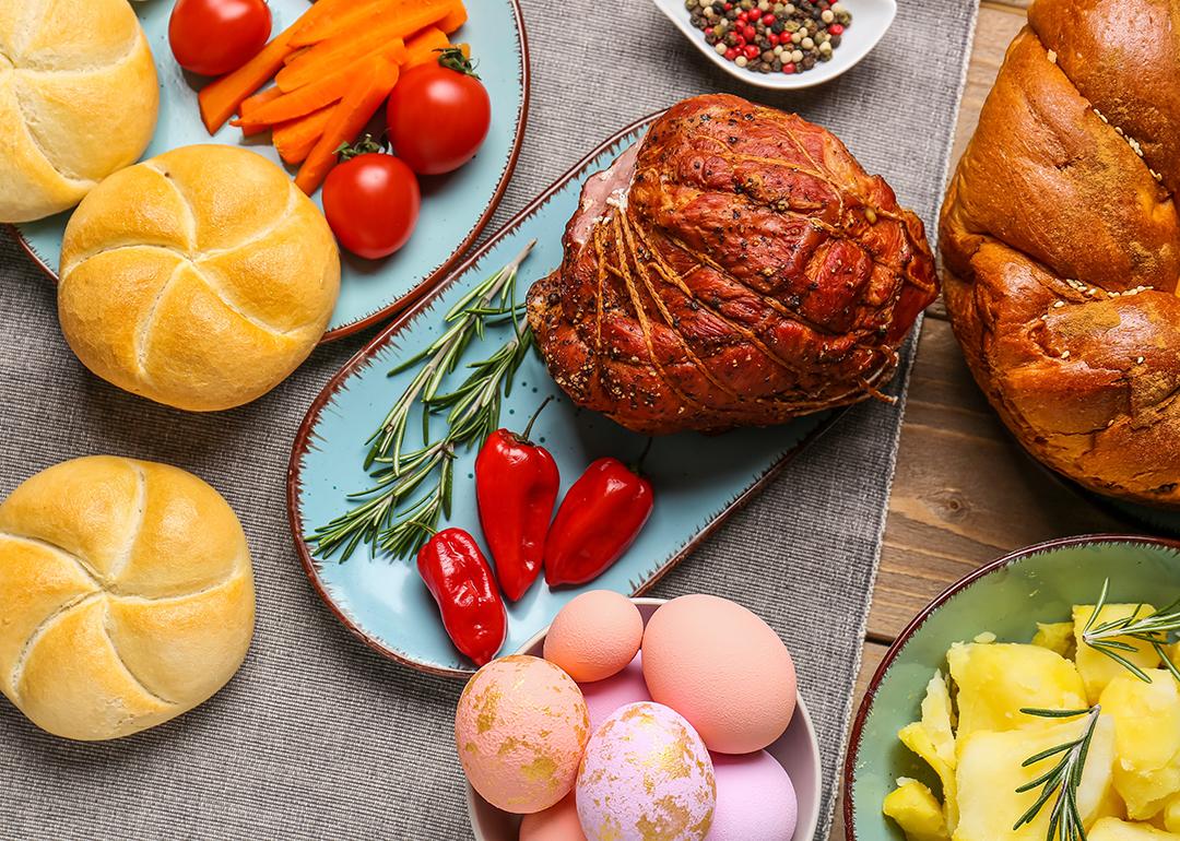 Easter dishes such as honey ham, baked buns, potatoes and colorful easter eggs on a wooden table.