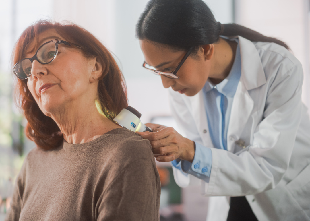 Dermatologist using a medical magnifying glass to inspect the skin of an elderly woman patient