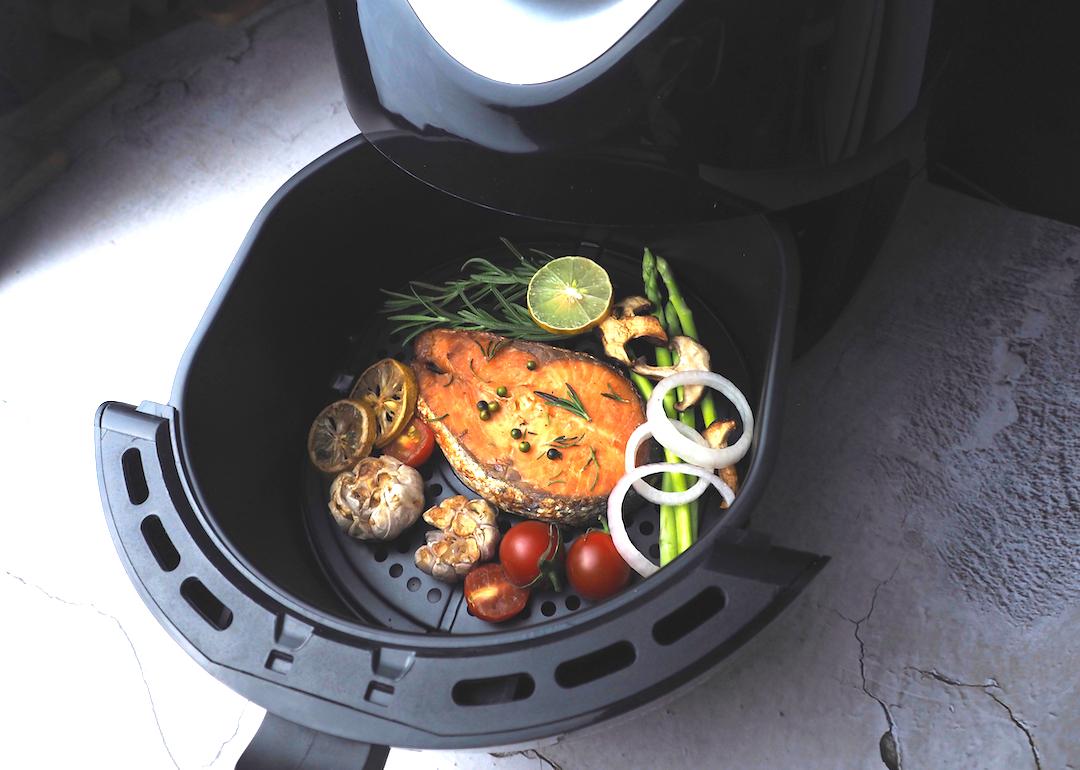 Salmon fillet with thyme, garlic, and lemon slices, mushrooms, and tomatoes in an air fryer.