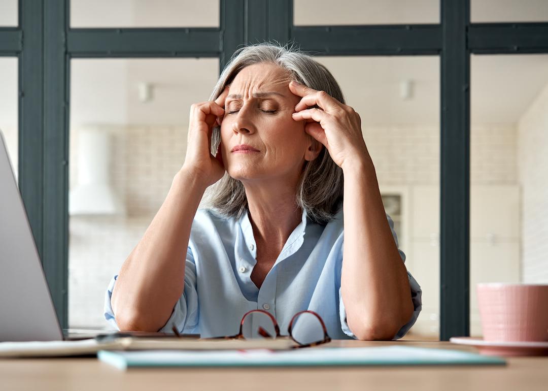 Senior person holds head in hands while at desk.