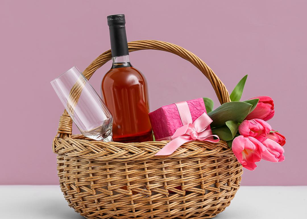A Mother's Day gift basket with a wine bottle, wine glass, a gift box and pink flowers.