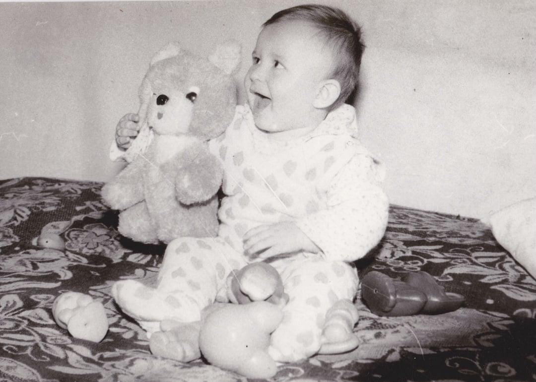 Old cute photo of a baby sitting with toys.