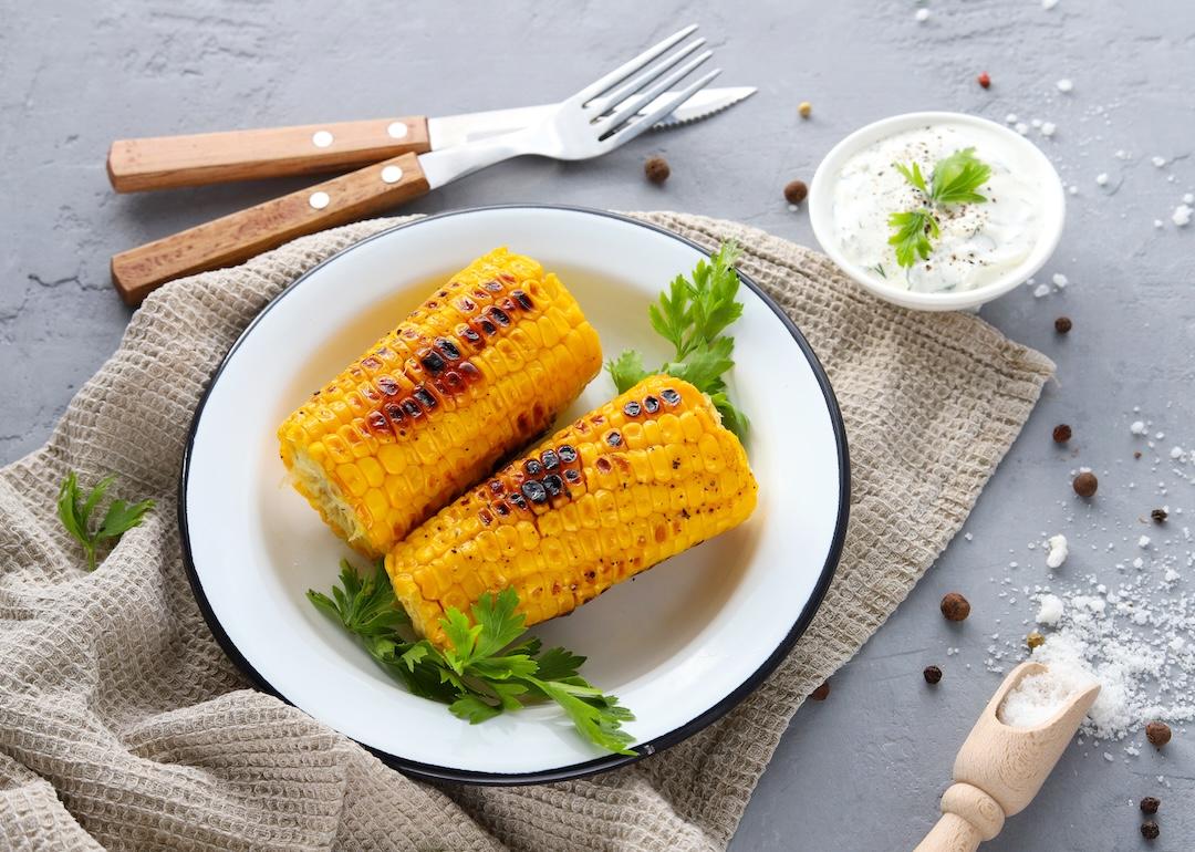 Grilled corn cobs with spices and sauce on a concrete background, top view.