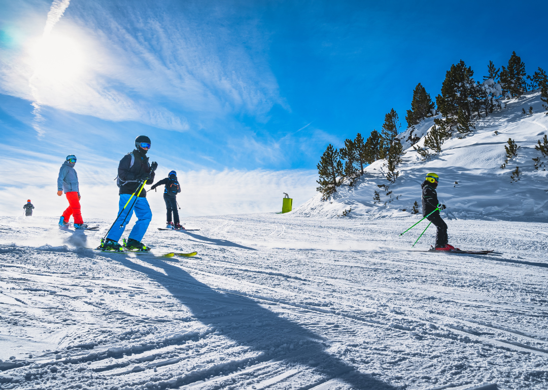 People skiing and snowboarding down a ski slope against a clear blue sky