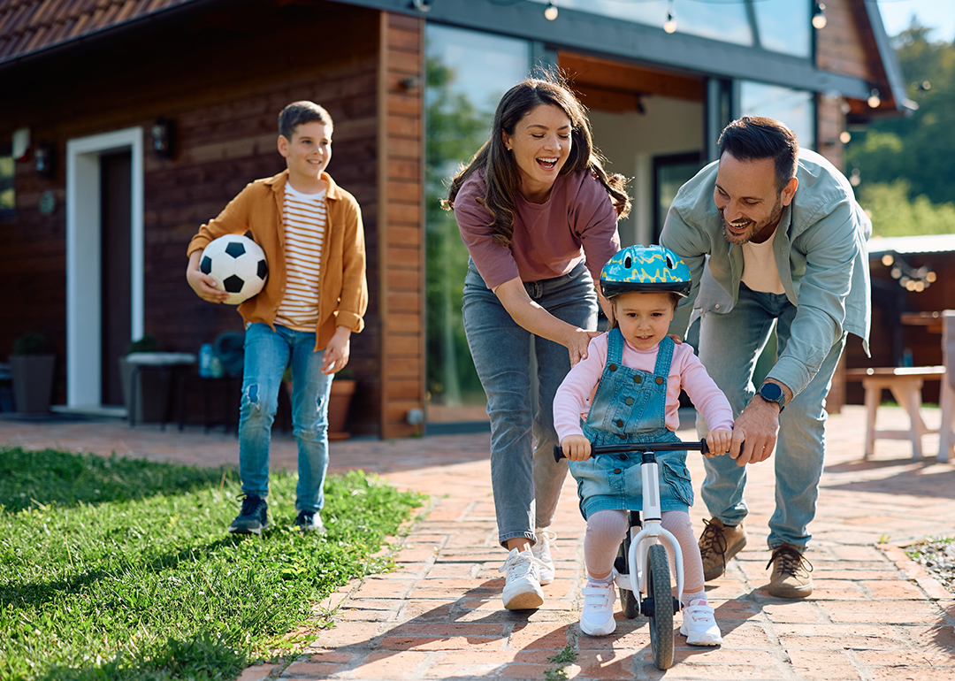 Child learning to ride bicycle with help of her parents.