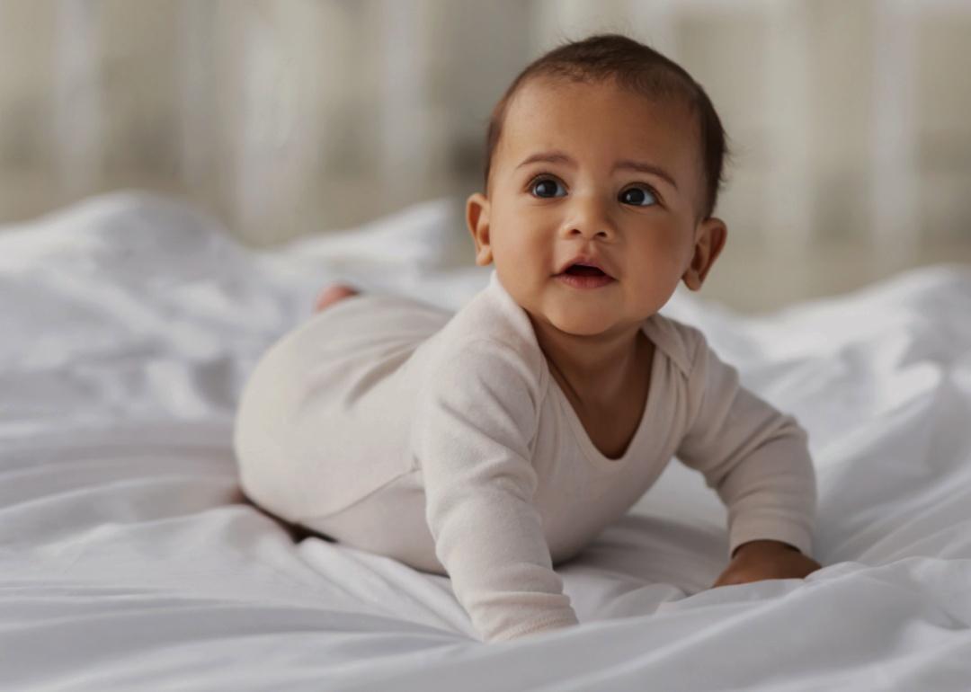 A baby lying on their stomach on a white bed.