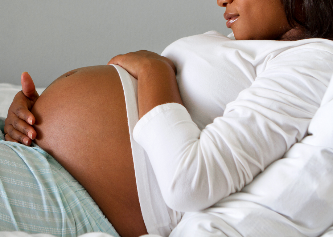 A pregnant person lying in a hospital bed cradling her stomach.