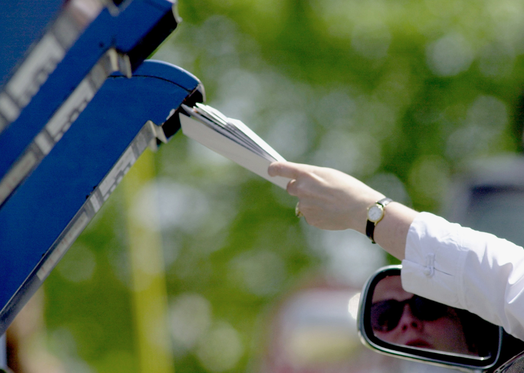 A woman deposits her tax return into a mailbox.