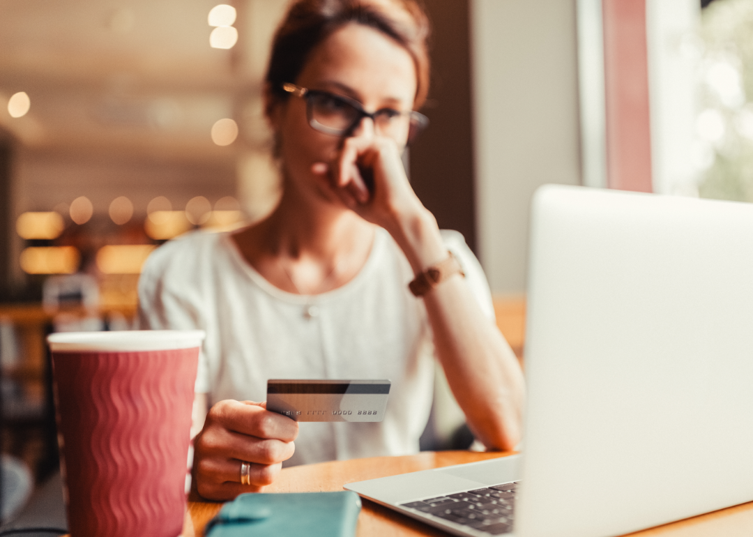 A woman holds a credit card and looks at her laptop with concern.