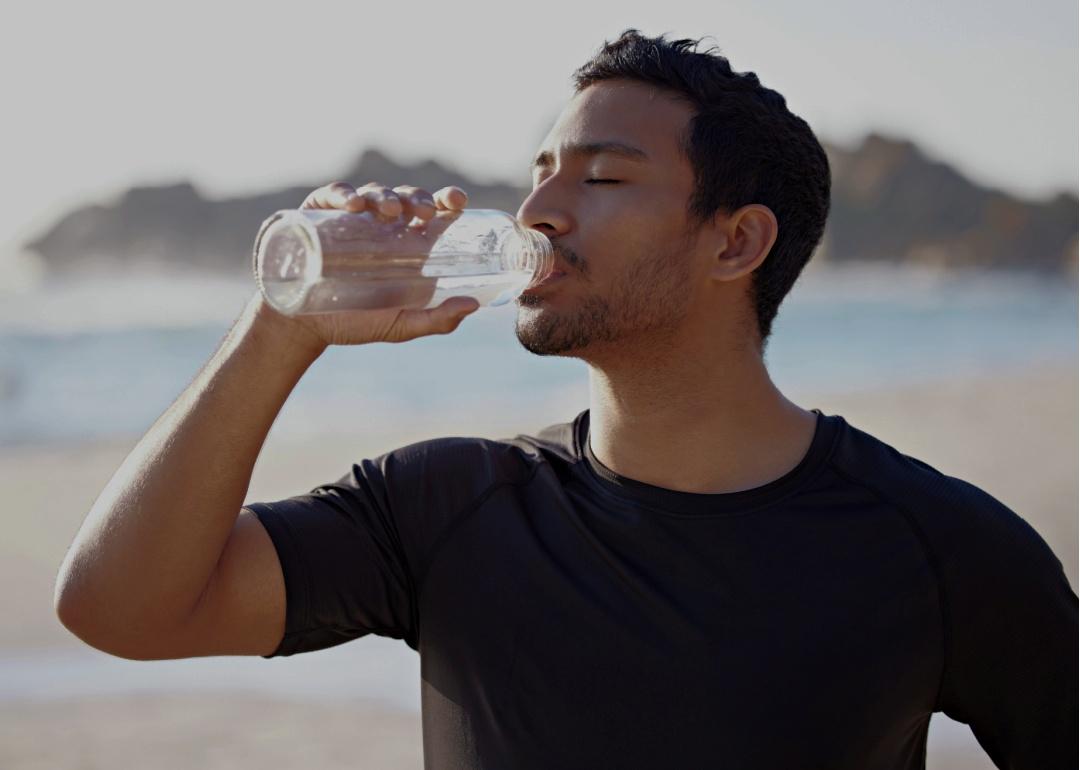 A young man tilting a water bottle to his mouth.