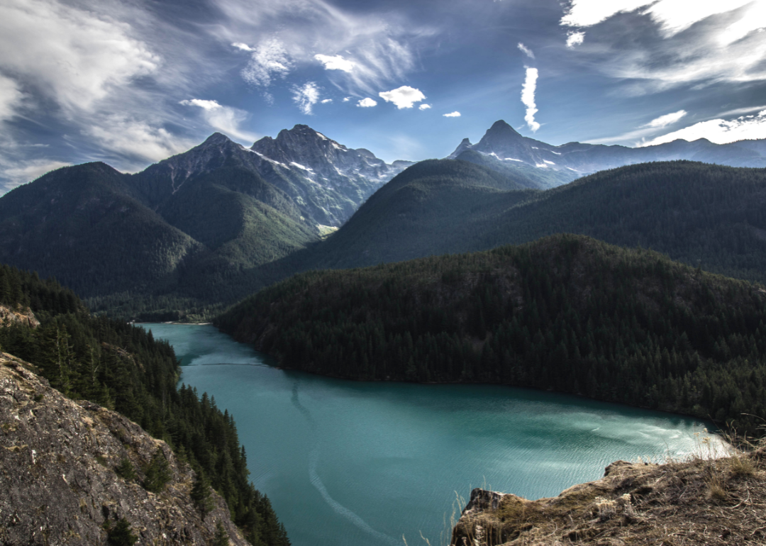A man takes a picture of a mountainscape with a lake in the distance. 