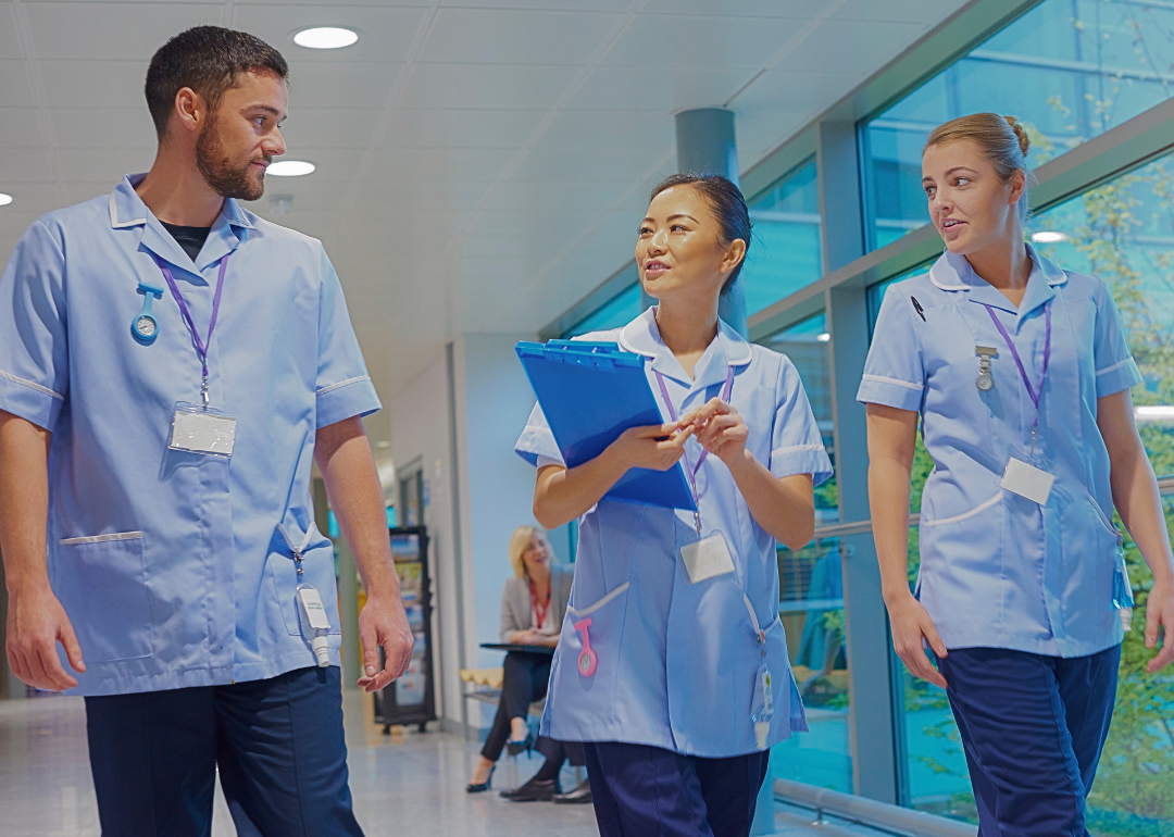 A male nurse and two female nurses walking in the hospital looking at the nurse in the center with a clipboard.
