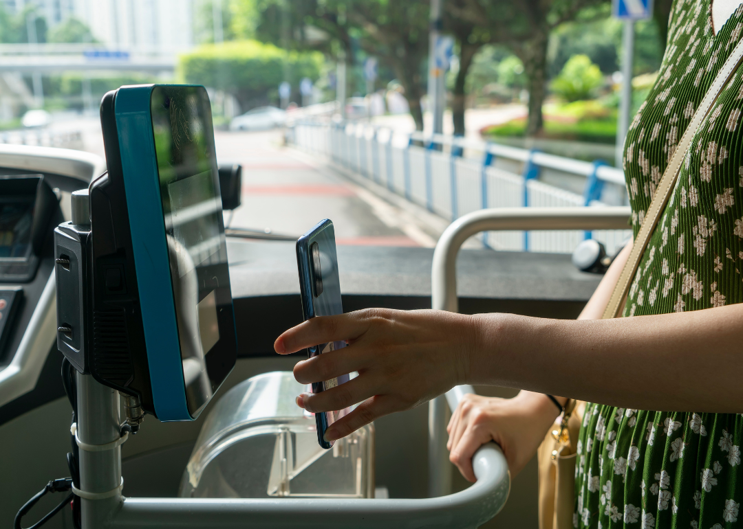 A person uses contactless payment on their smartphone to pay for their bus fare as they board.