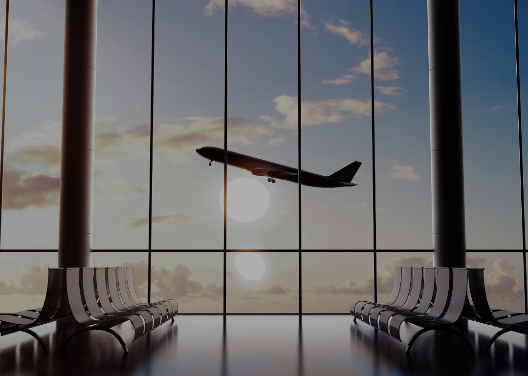 An airport terminal building with rows of empty chairs and airplane seen through the windows.