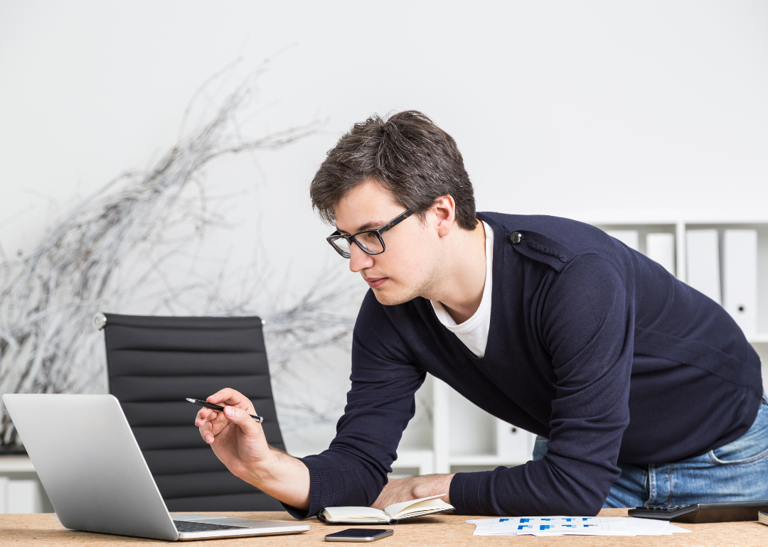 A man leaning on a desk and looking into computer.