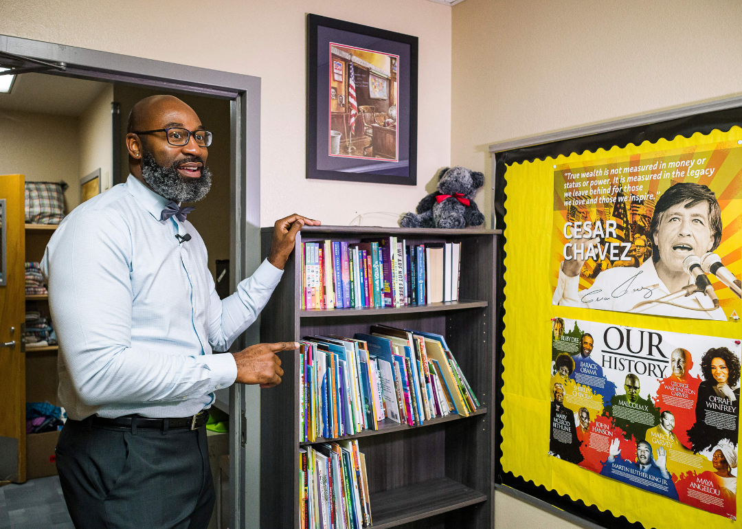 A teacher speaking in his classroom, pointing to posters featuring Black history icons figures and Cesar Chavez. 
