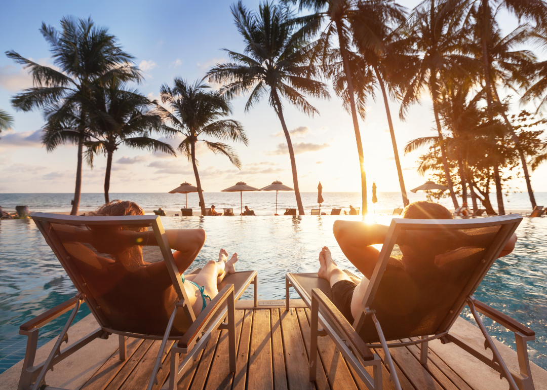 Two people sitting in chairs by a pool overlooking the ocean.