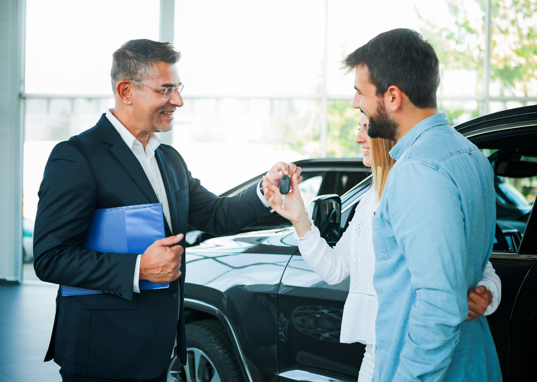 A couple being handed the keys to a new car at a car dealership