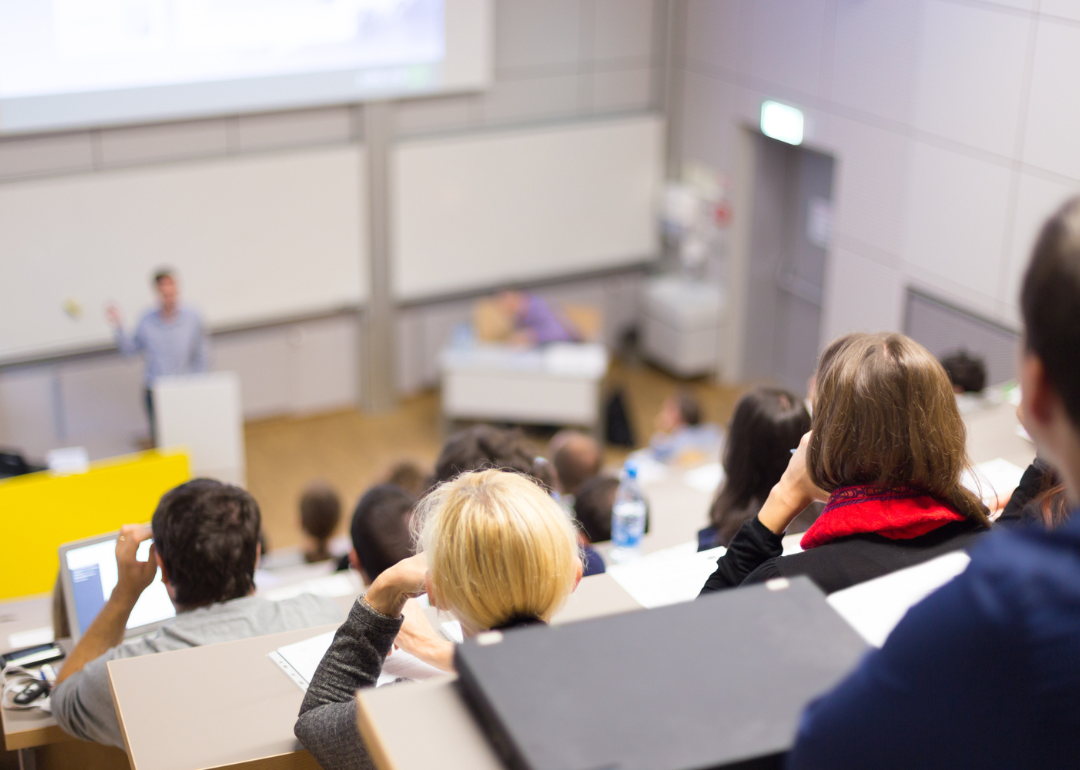 Students listening to their professor speak in a large lecture hall.