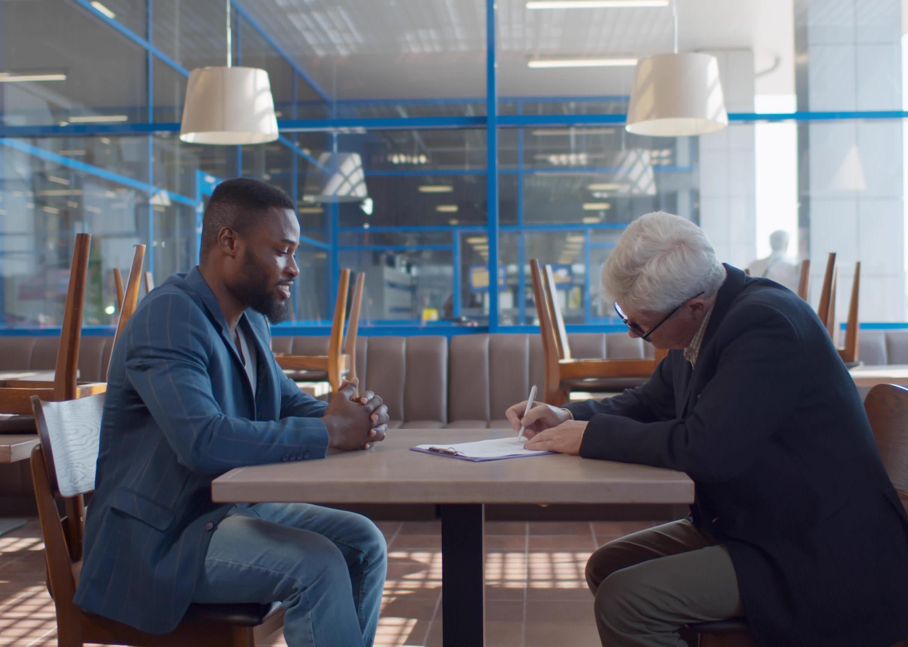 Two men signing paperwork in a restaurant with chairs on the tables.
