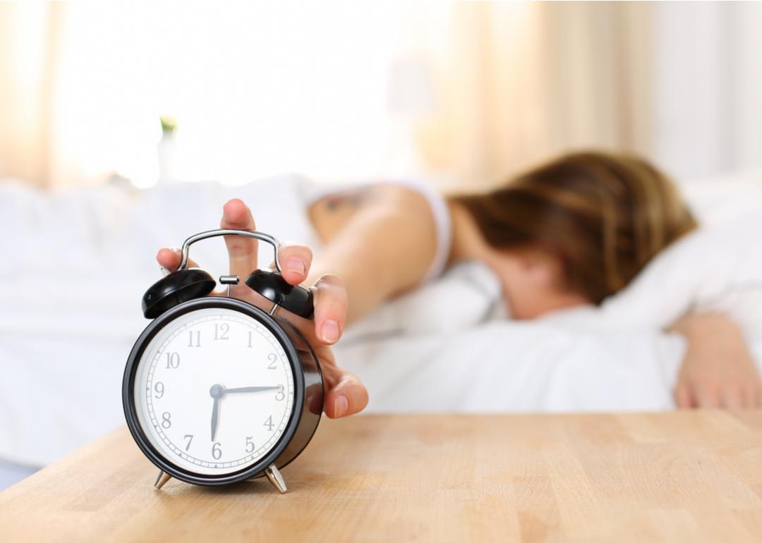 Woman hitting alarm from bed.