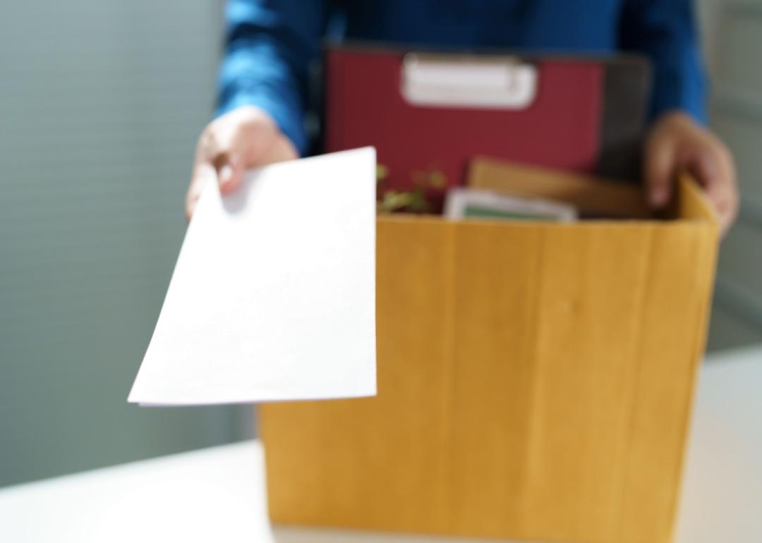 A person with a packed box handing in a resignation letter.