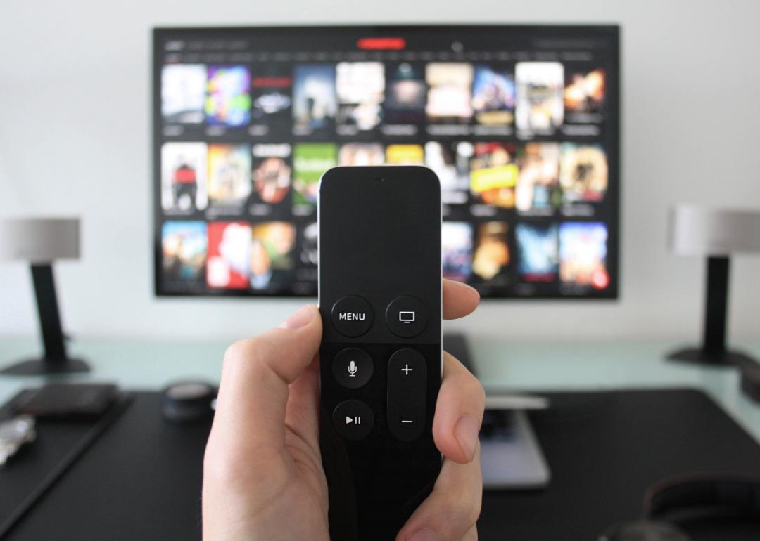 Hand holding a TV remote while watching shows on a streaming service.