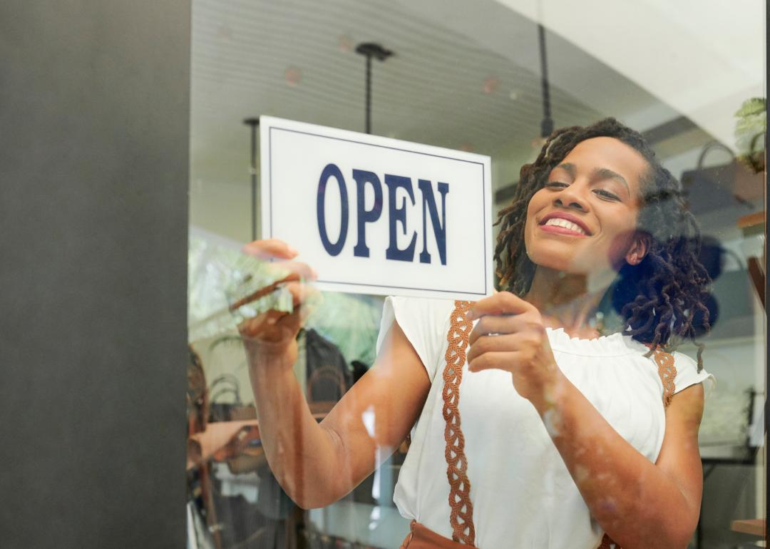 Young woman turning around the open sign on her shop's door.