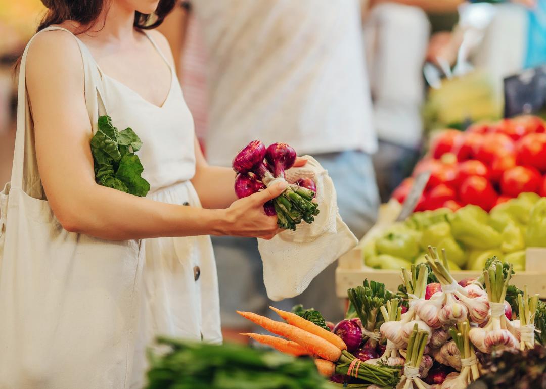 Hands putting fruits and vegetables in a cotton produce bag at food market. 