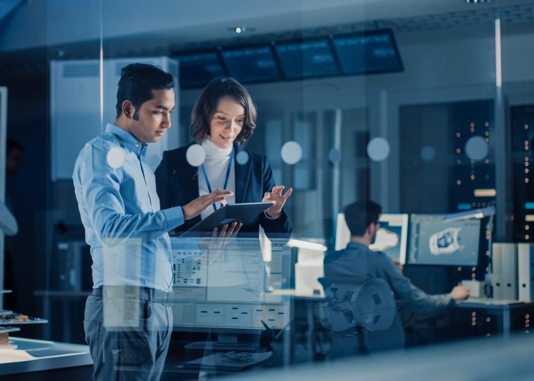 Two employees chat over a tablet in a tech lab.