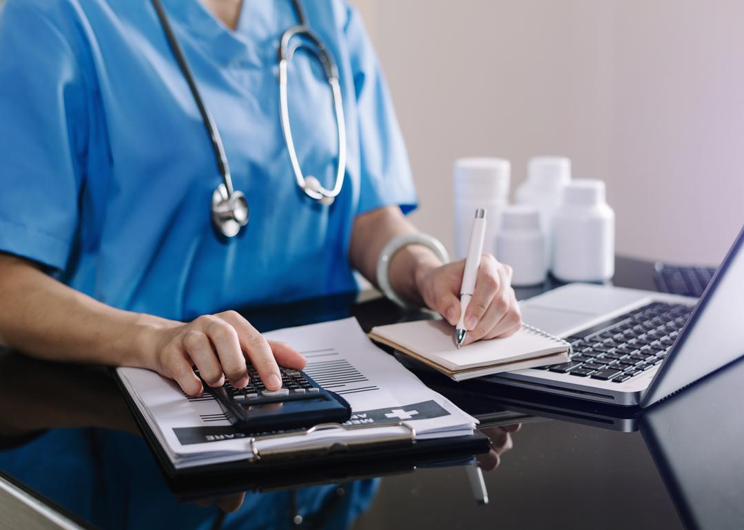 Hand of a health care worker using a calculator and notepad.