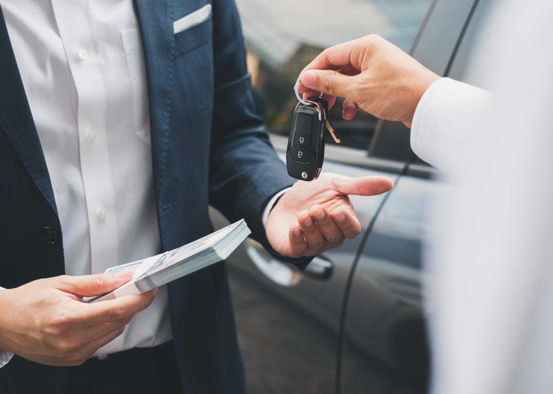 Closeup of a hand giving a car key in exchange for money.