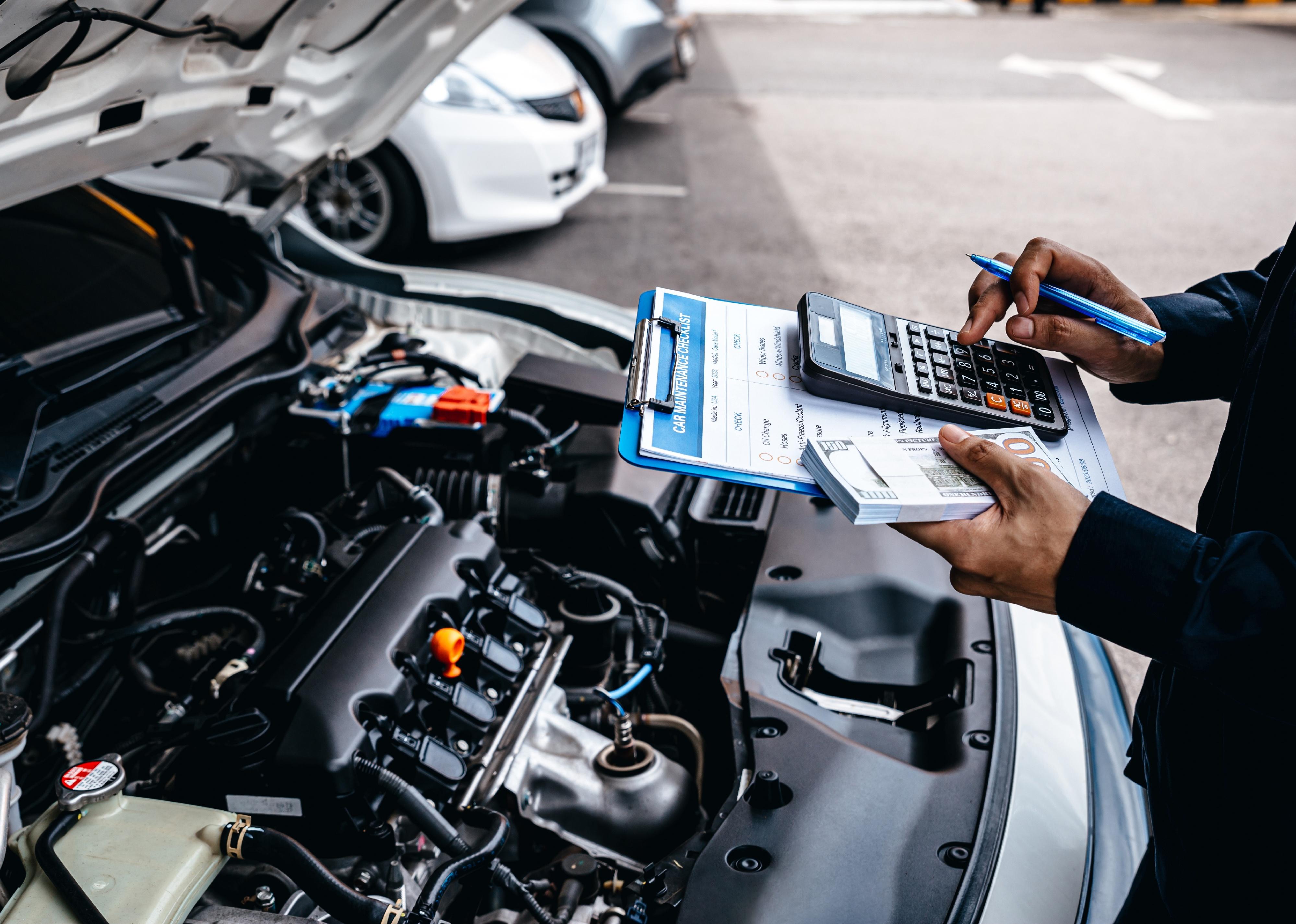 Mechanic calculates the cost of car repairs to customer at garage workshop.