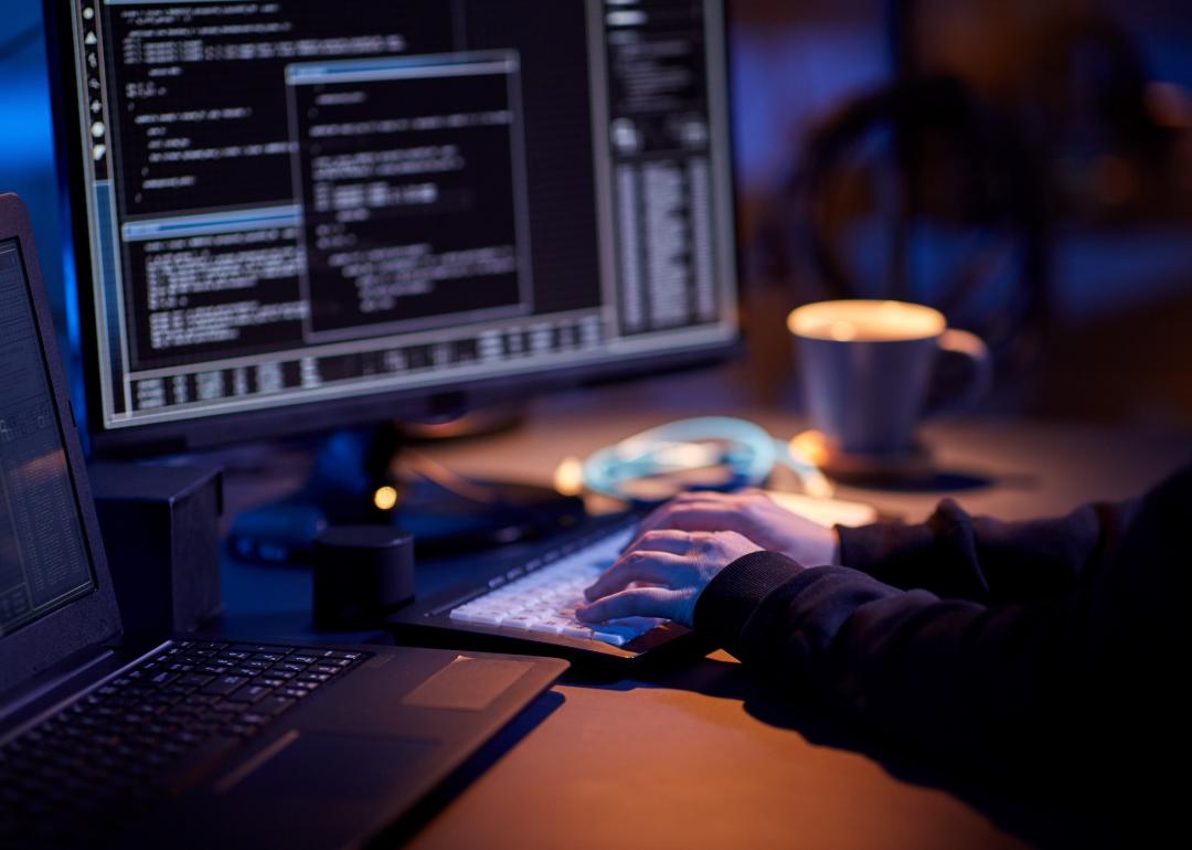 Close up of hacker in dark room writing code.