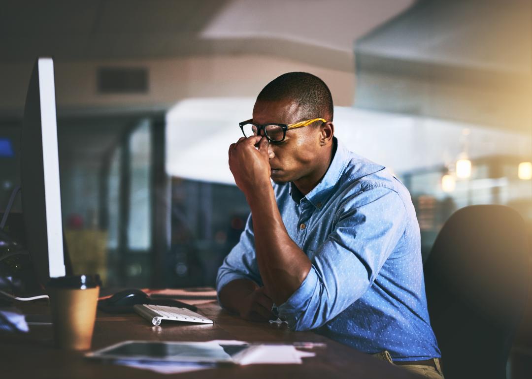 Stressed businessman pinching nose at night in office.
