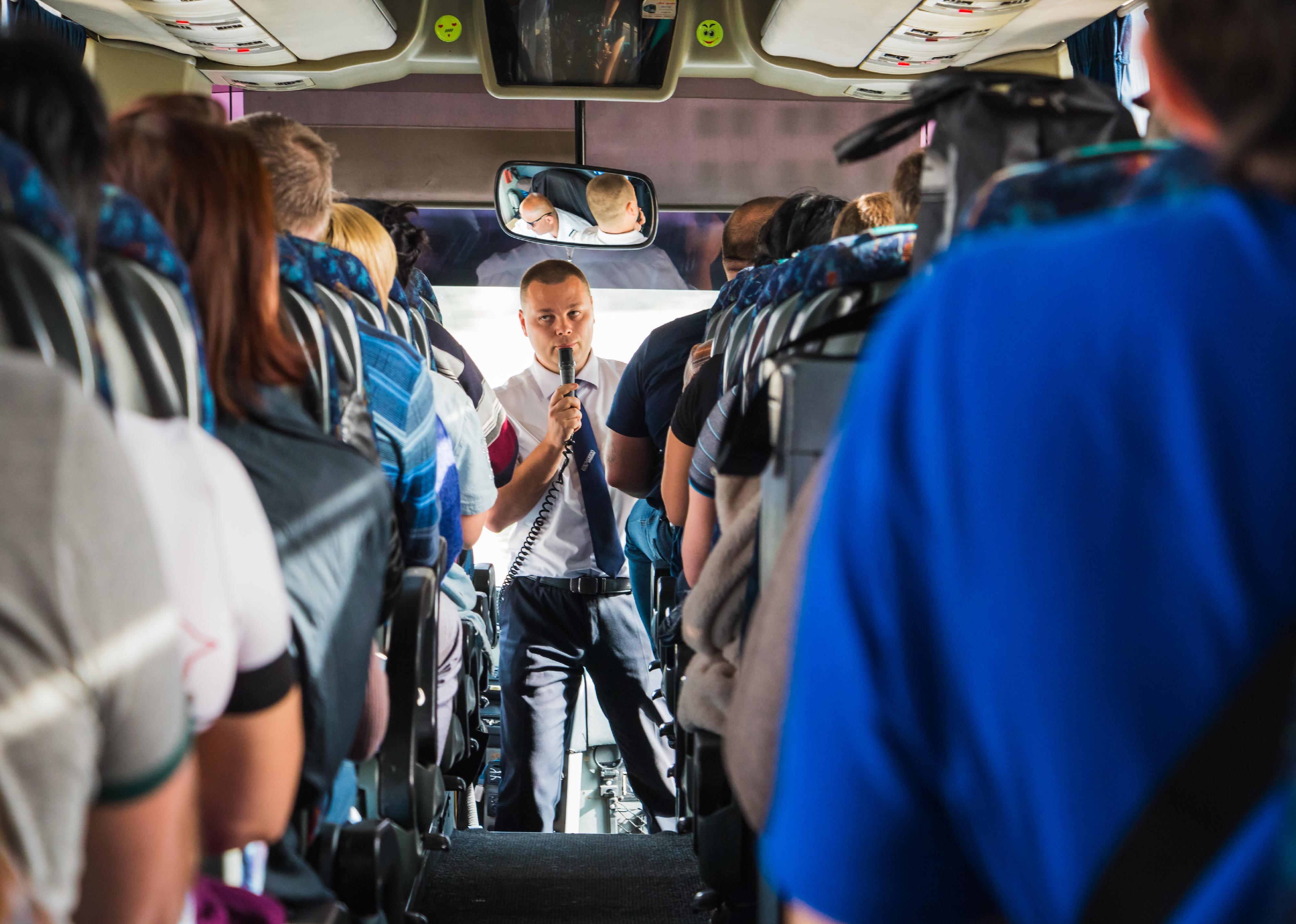 Tourists and a male tour guide with a microphone in the bus