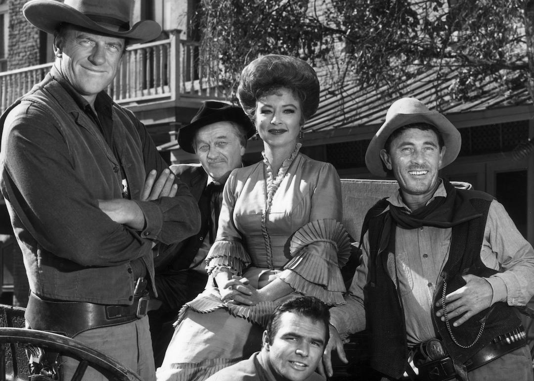 The cast of 'Gunsmoke' poses around a wagon in a promotional portrait for the Western television series. From left to right are actors James Arness, Milburn Stone, Amanda Blake, Ken Curtis, and Burt Reynholds is on the second row.