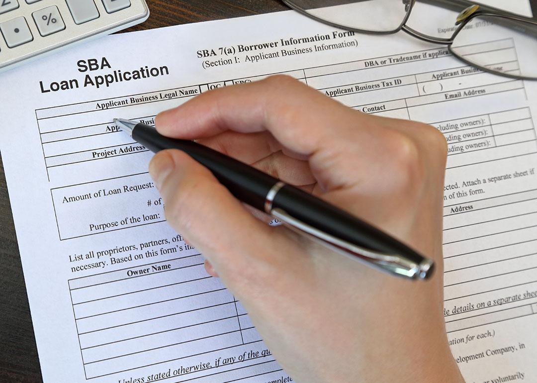 Person filling out paper SBA loan application form by hand.