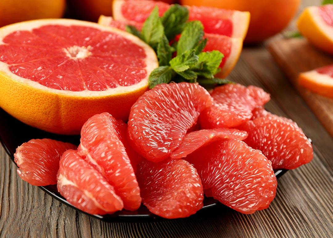 Beauty photo of sliced half a grapefruit on a black plate with peeled pieces of grapefruit in the foreground. 