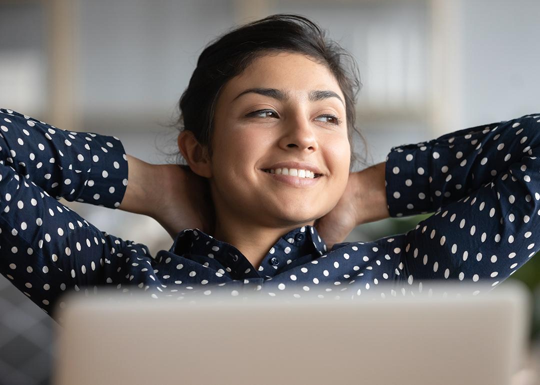 Satisfied woman happily sitting  at work with her hands behind her head.