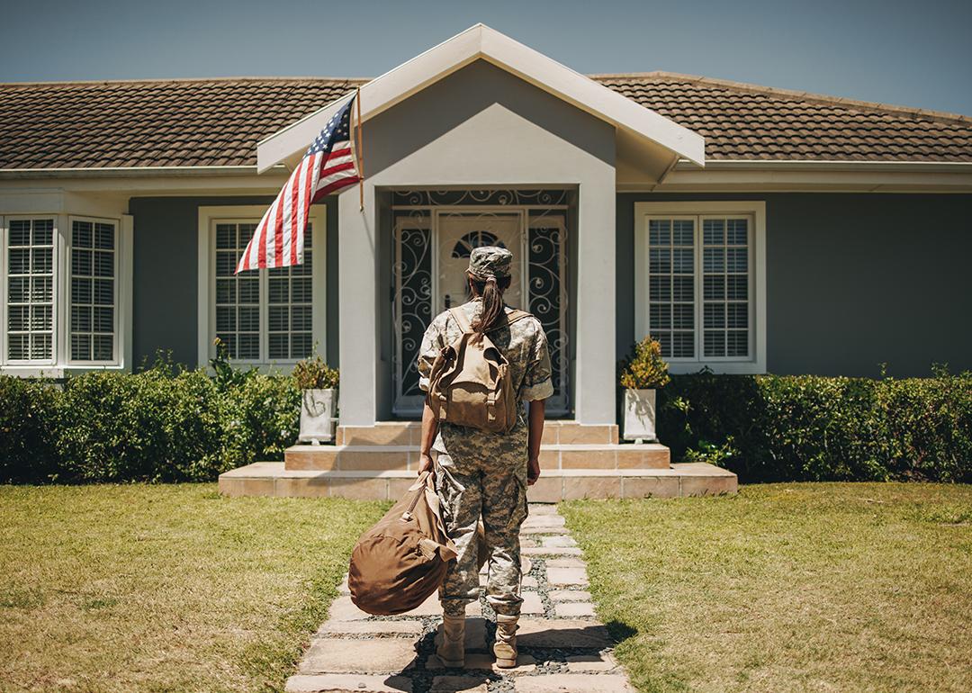 Female veteran soldier with luggages coming home and standing in front of her house.