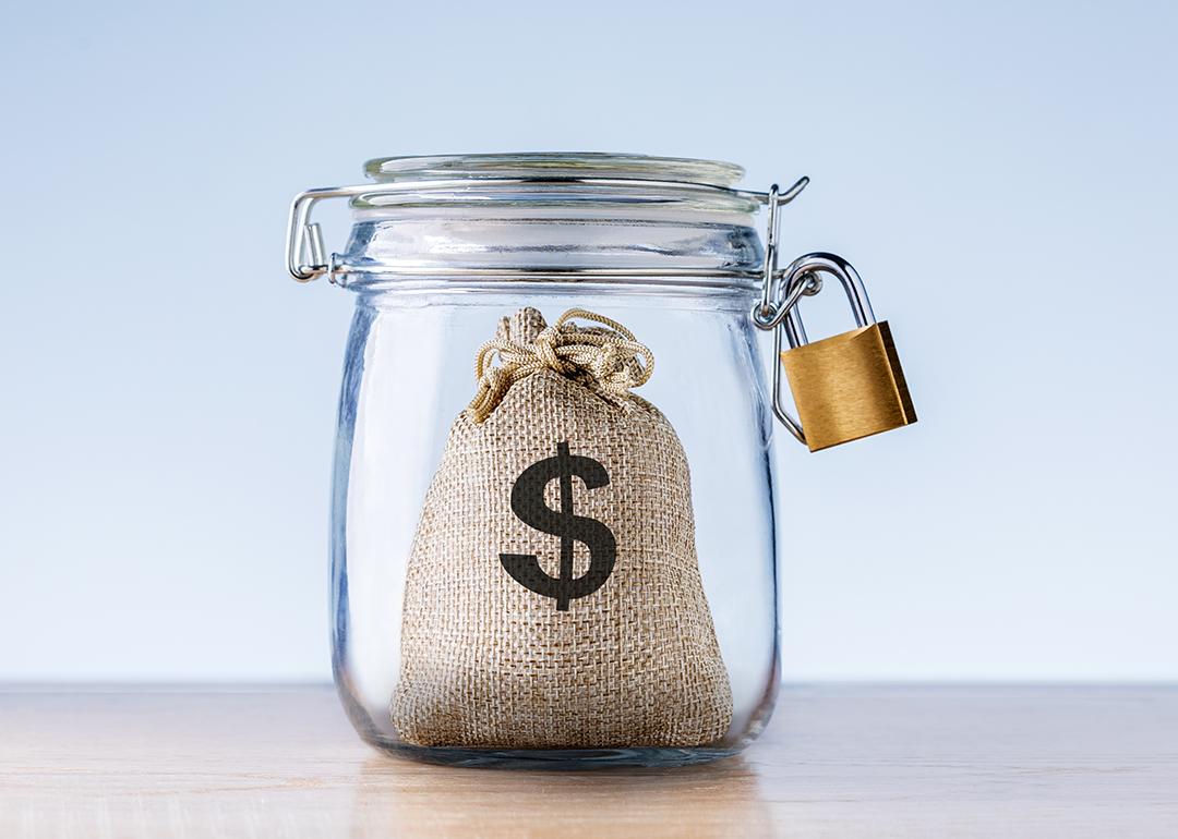 Concept of an emergency fund - a mini bag with a dollar symbol on it locked inside a jar.