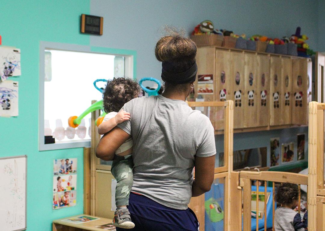 A child care teacher carrying an infant in a child care room.
