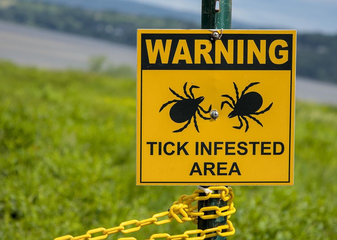 A yellow warning sign telling people of a tick infested area in a grassy area near the Hudson river in Westchester County, New York.