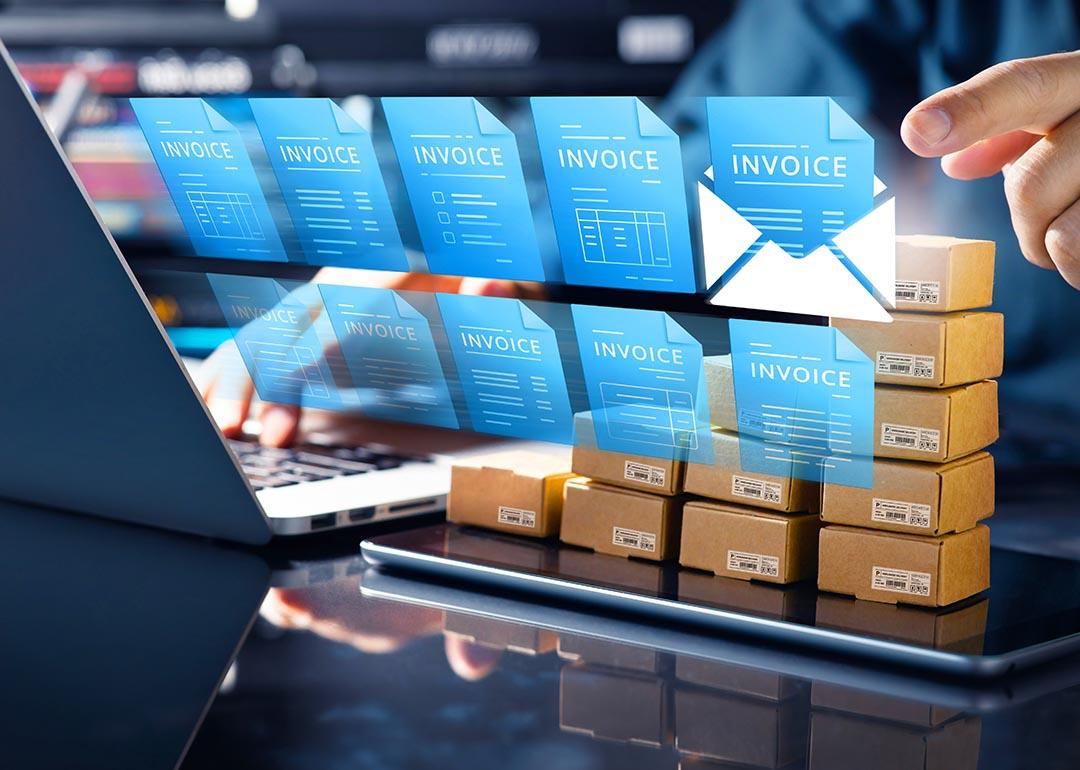 Concept of technology in accounting illustrated by 10 blue virtual invoice icons superimposed over person using a laptop computer.