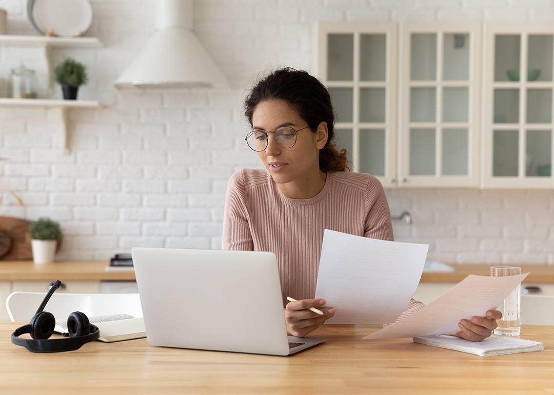 Young female at home using a laptop and reading financial documents.